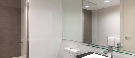 Une salle de bain moderne avec une douche à parois de verre, des toilettes blanches et un grand lavabo surmonté d’une étagère en verre.