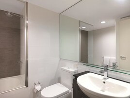 Un baño moderno con ducha de vidrio, inodoro blanco y un lavamanos grande con un estante de vidrio arriba.