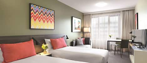 A hotel room with two beds, a desk, a chair, a TV, and a window with curtains.