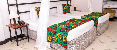 A hotel room with two beds, a bedside table with a lamp, a telephone, and a basket.