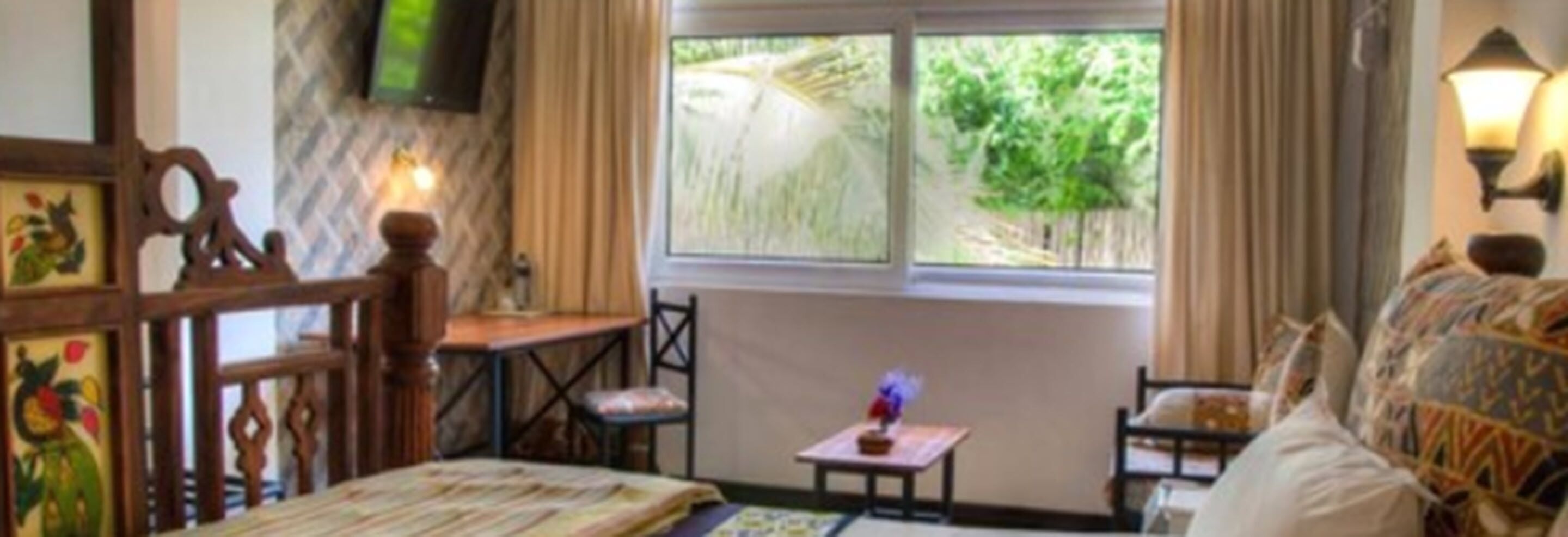 A cozy room with a bed, a small table with a vase, and a window with a view of greenery.