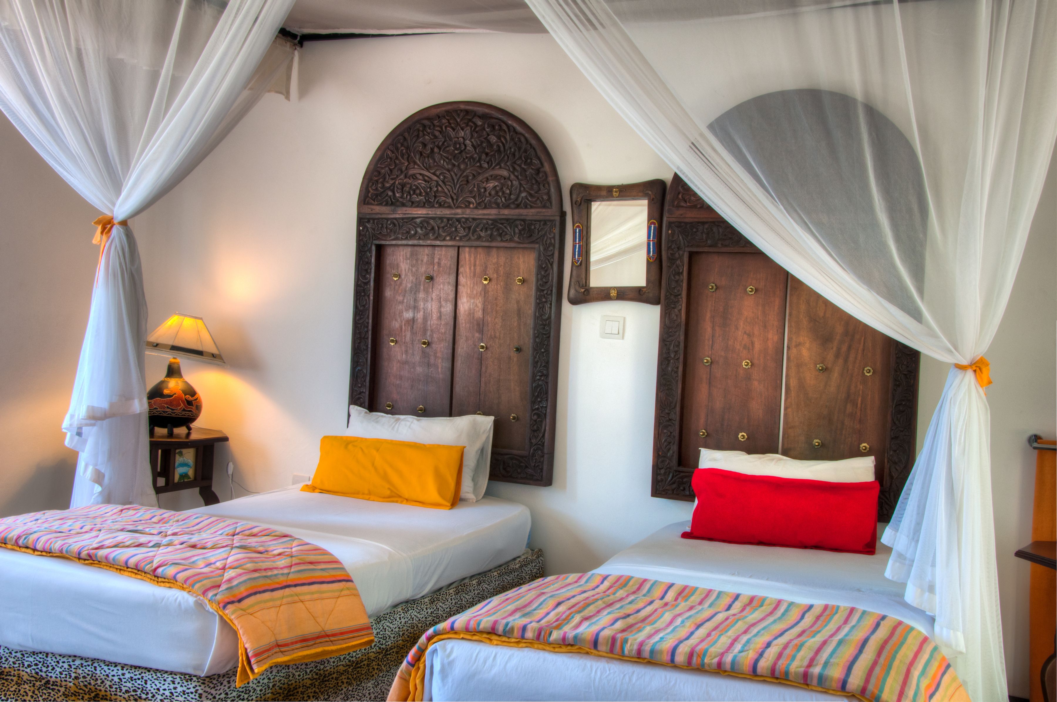 A room with two beds, each with a canopy, a wooden headboard, and a mirror.