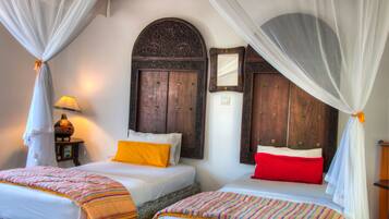 A room with two beds, each with a canopy, a wooden headboard, and a mirror.