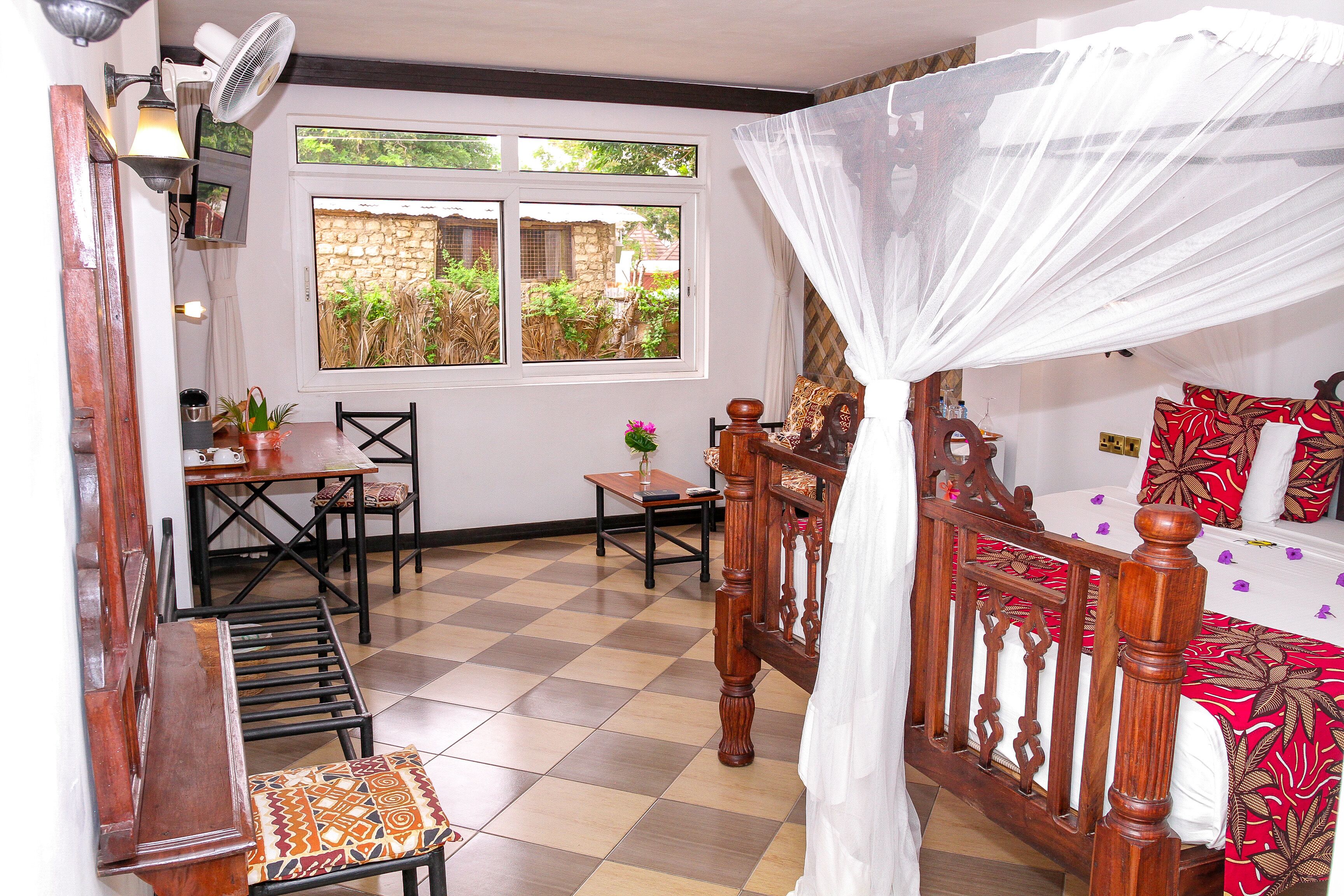 Una habitación con cama, una mesa de comedor, sillas, una mesita con una planta y una ventana con vistas a zonas verdes.
