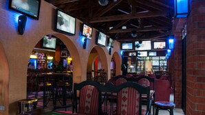 A restaurant with multiple TVs on the wall, wooden beams, and brick walls.