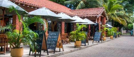 A restaurant with outdoor seating, potted plants, and a red-tiled roof.