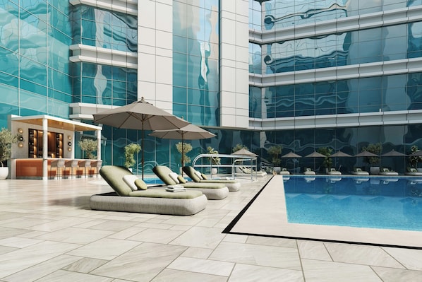 A modern indoor pool area with lounge chairs and umbrellas, surrounded by reflective glass walls. - Marriott Hotel Production City, Dubai (Dubai)