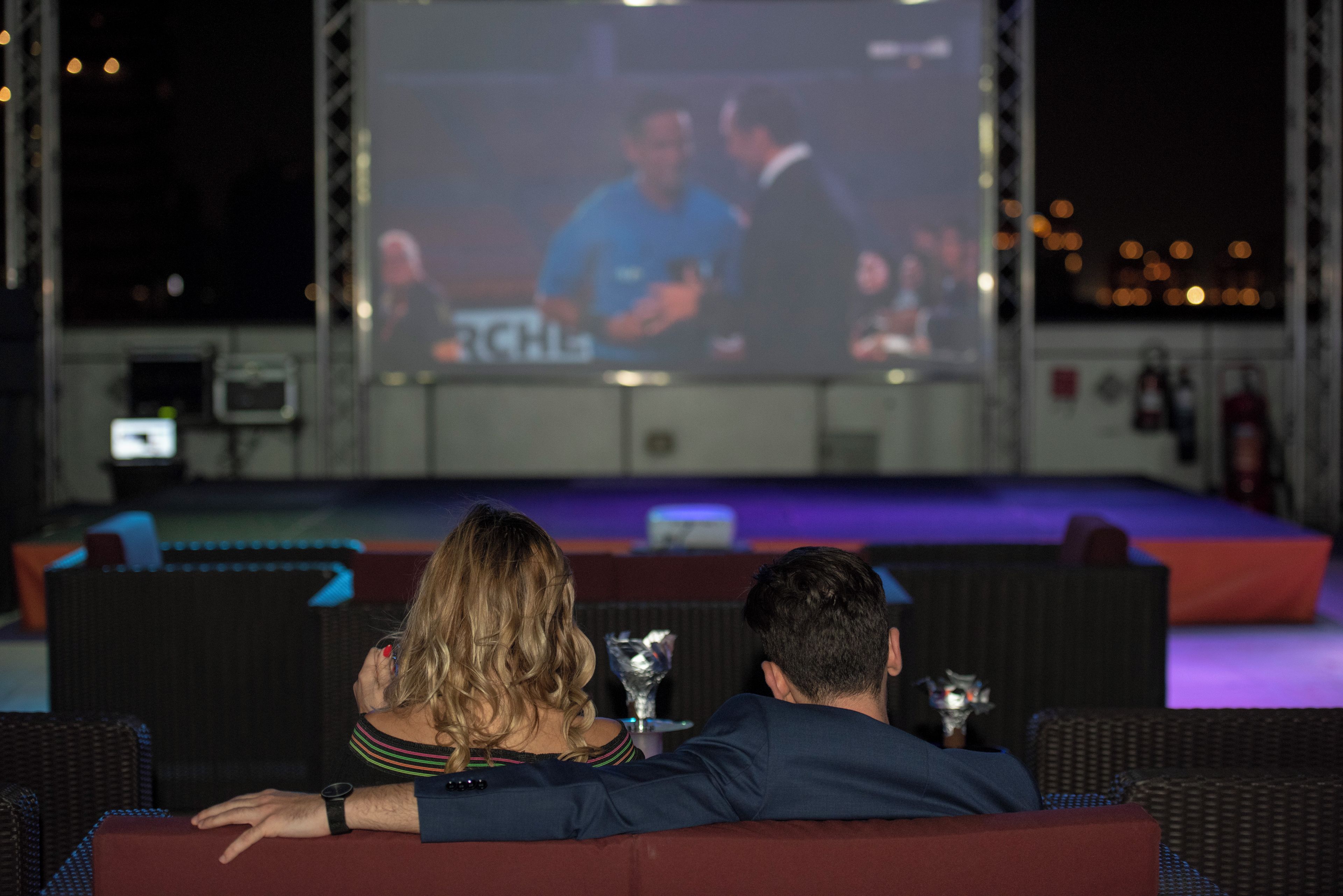 Cine al aire libre con una pantalla grande, asientos y escenario.