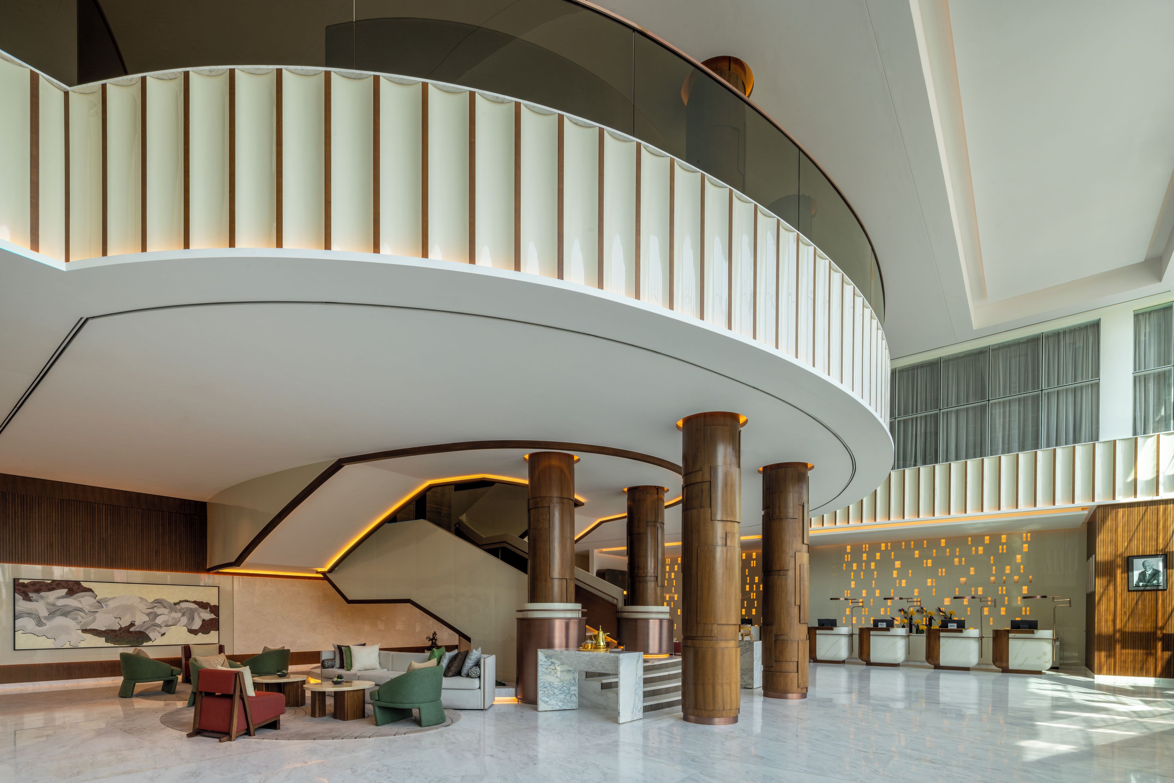 A spacious lobby with a curved staircase, seating area, reception desk, and a large artwork on the wall.