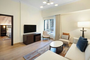 A modern hotel room with a large window, a flat-screen TV, a sofa, a chair, a small table, and a TV stand. - Marriott Hotel Production City, Dubai (Dubai)
