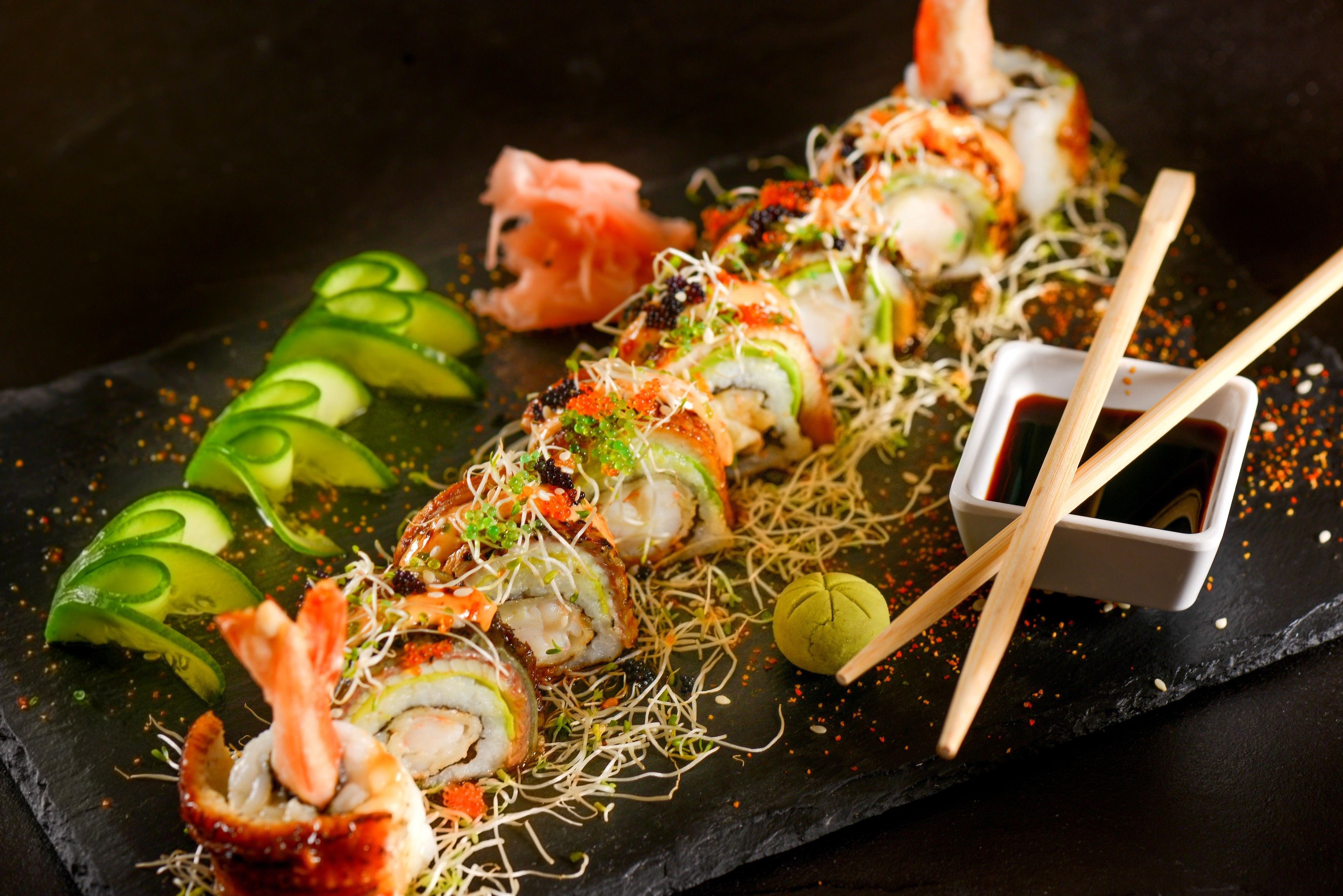 Sushi-Rollen mit einer Dipsoße und Essstäbchen auf einer Schieferplatte.