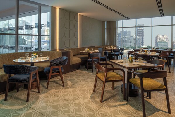 A modern restaurant with high ceilings, large windows, and a city view.