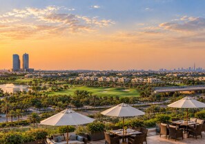 A rooftop terrace with outdoor seating and umbrellas, overlooking a golf course and city skyline.
