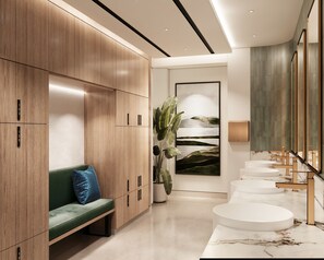 A modern hotel lobby with wooden lockers, a green bench, a large potted plant, and a marble reception desk. - Marriott Hotel Production City, Dubai (Dubai)