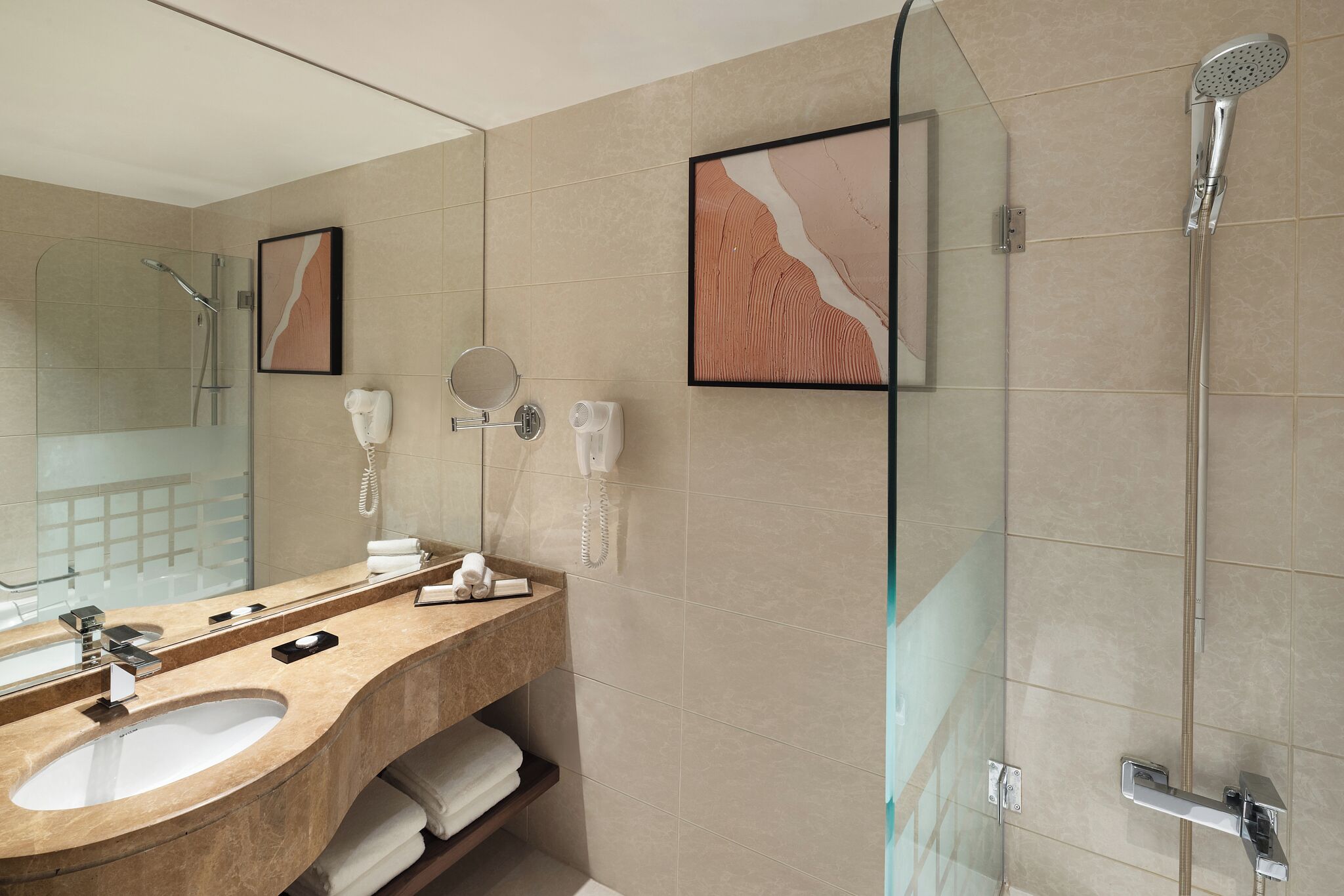 Une salle de bain moderne avec un grand miroir, deux lavabos, une douche et une œuvre d’art encadrée accrochée au mur.