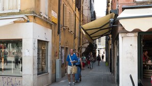 A narrow street with buildings on either side, a café with outdoor seating, and a few pedestrians. - Backpackers House Venice - Hostel (Venice)