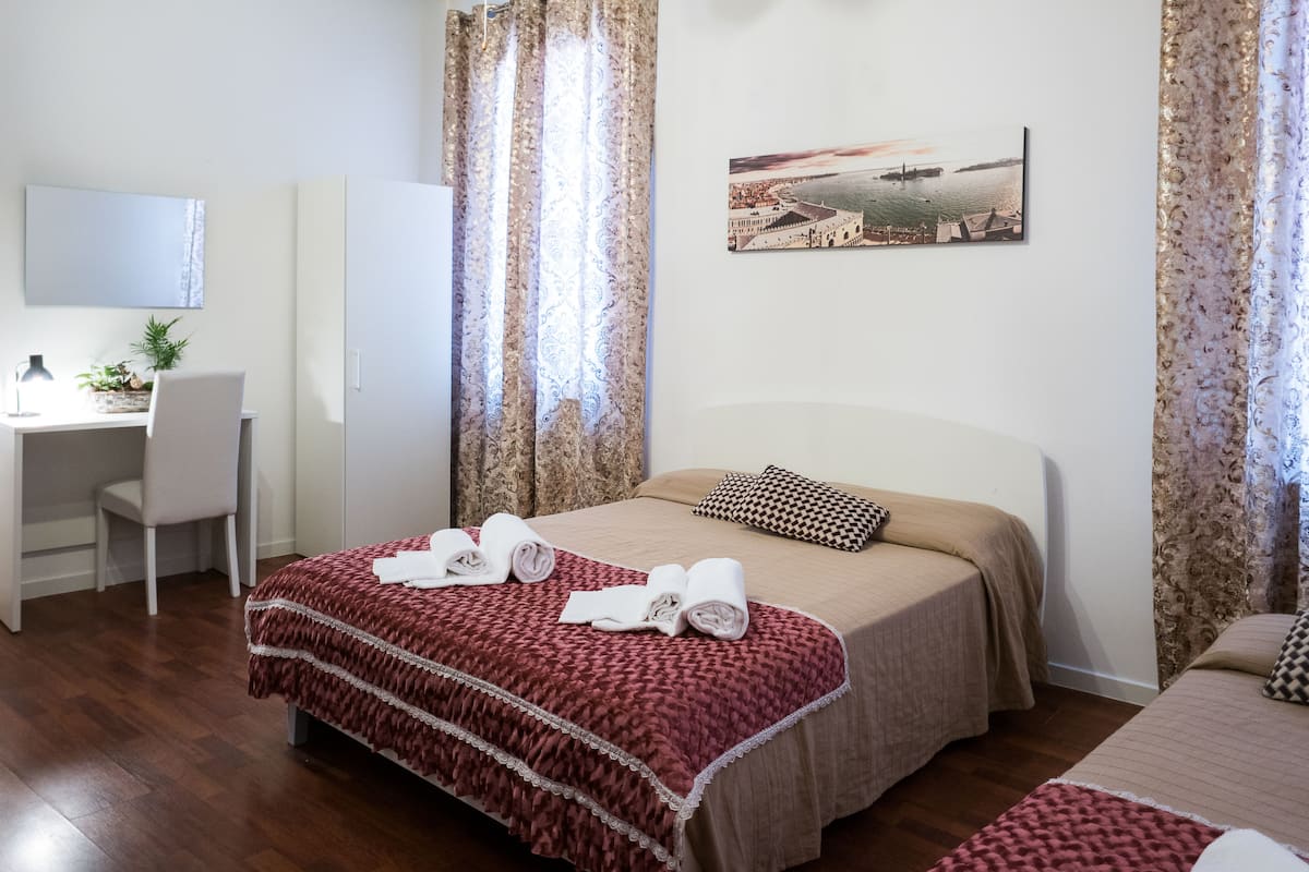 A hotel room with a bed, a desk, a chair, and a painting on the wall.
