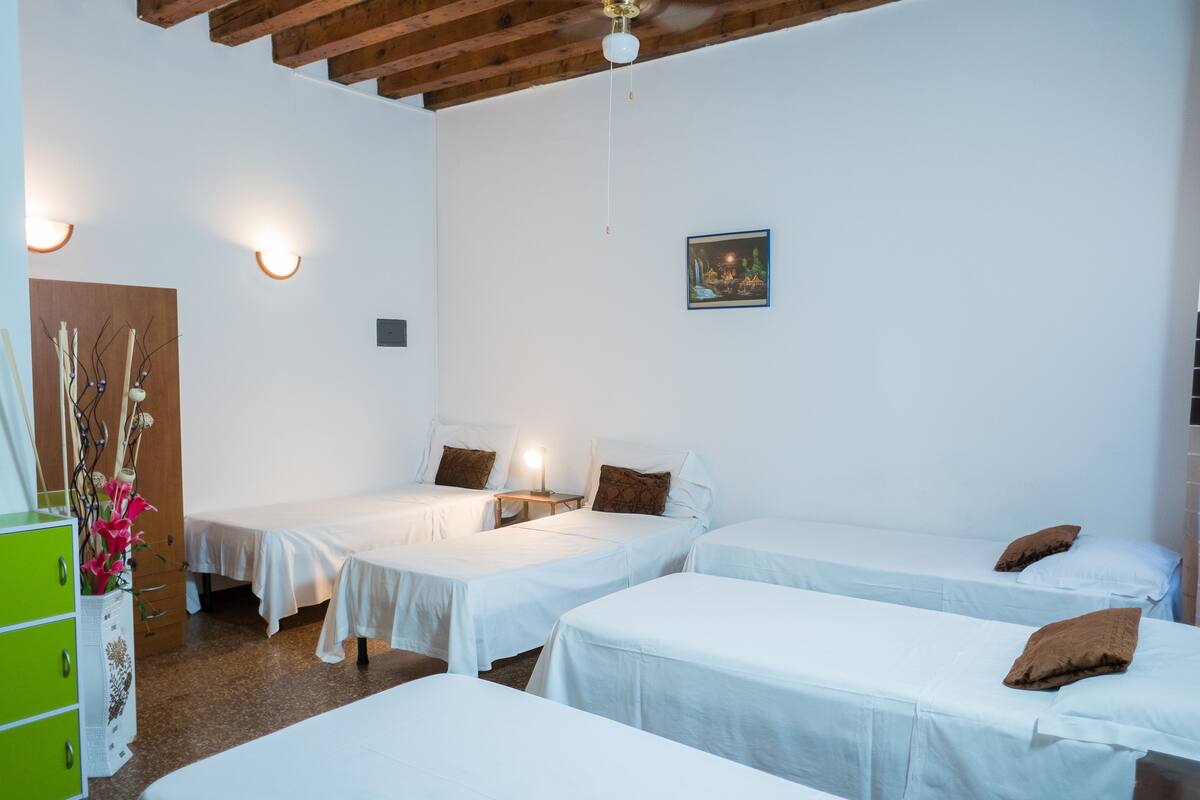 A hotel room with three single beds, a wooden ceiling, a green dresser, and a vase of flowers.