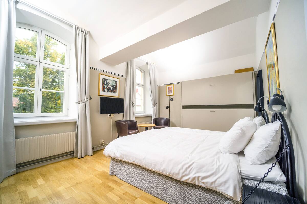 A hotel room with a large bed, a desk, a chair, a TV, and a window with curtains.