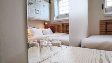 A hotel room with a wooden headboard, a bed with white bedding, a small table with glasses, and a window with blinds.