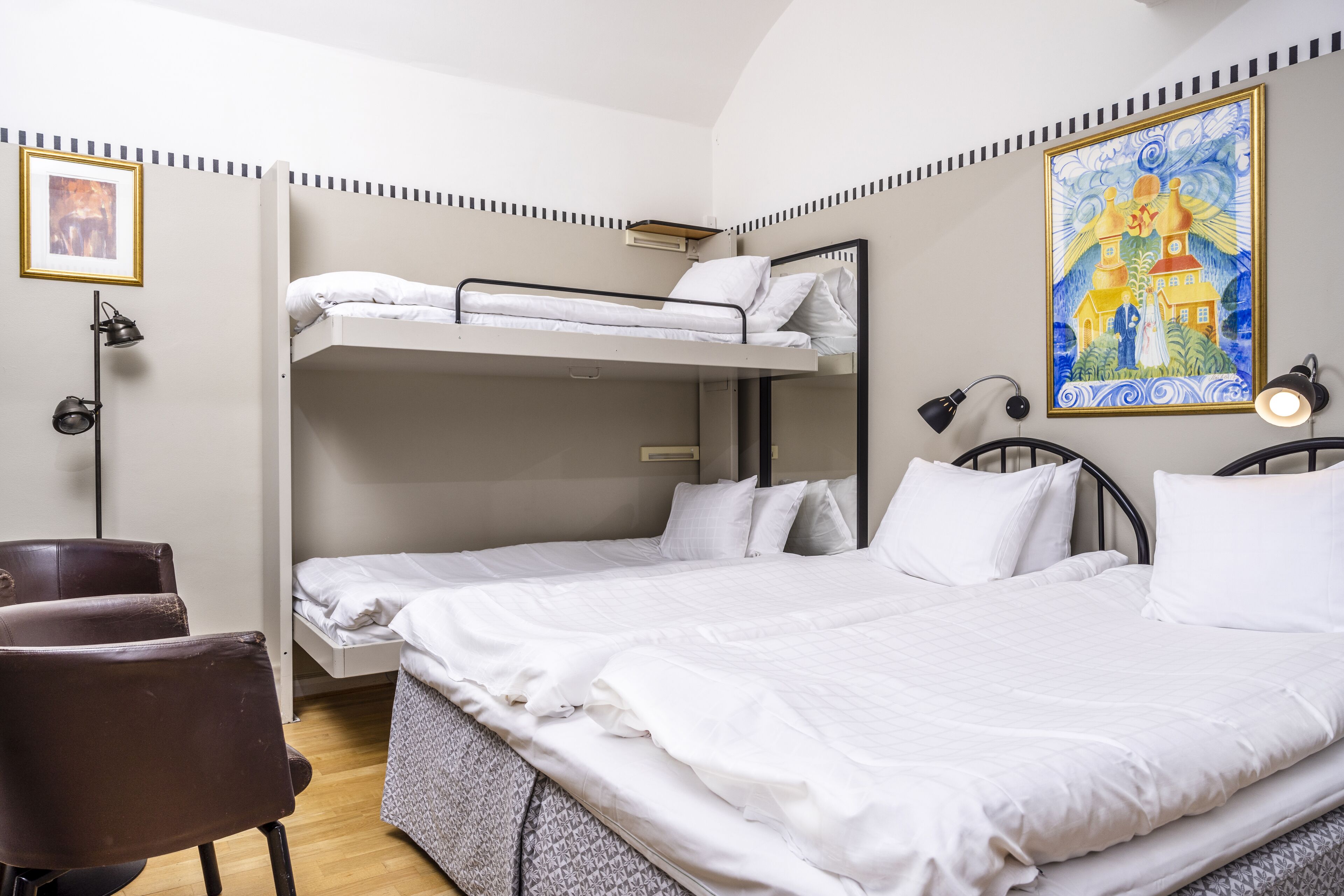 Habitació amb lliteres, una taula, una cadira, un quadre al mur i una pintura.