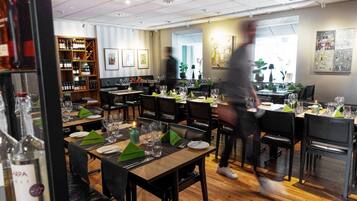 A restaurant with multiple tables set for dining, a wine rack in the background, and a person walking by.
