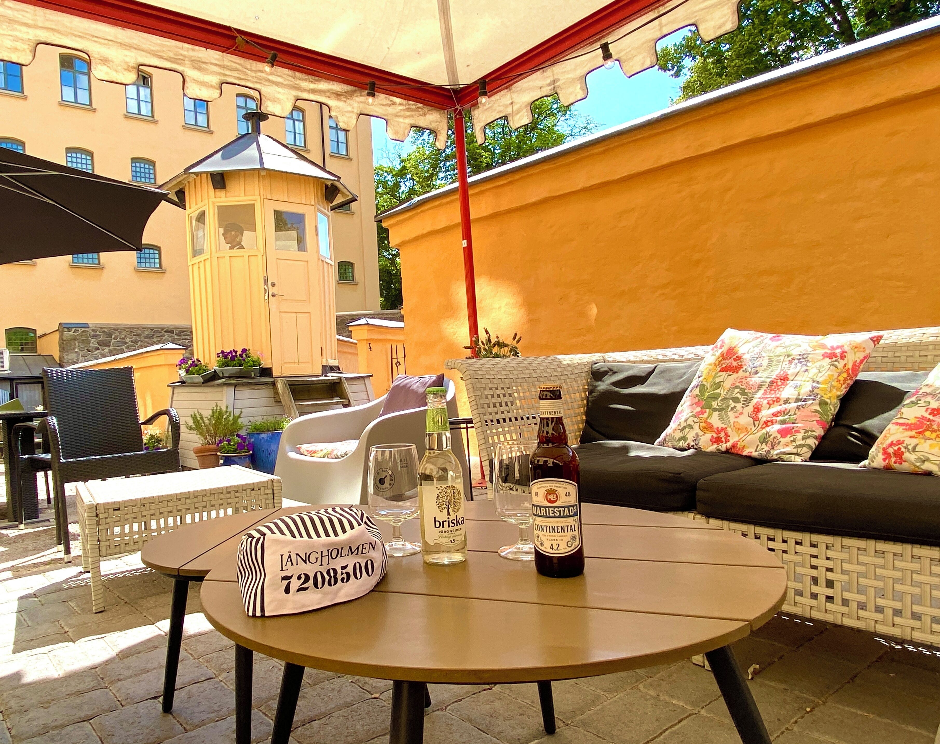 Ein Außenbereich mit Sitzgelegenheiten, darunter ein Tisch, Stühle und eine Couch. Auf dem Tisch stehen Flaschen und Gläser.