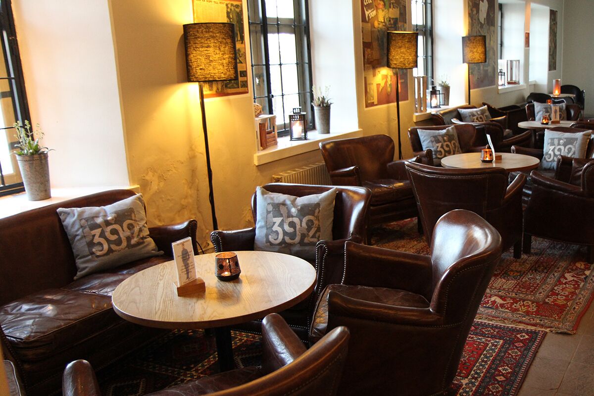 Un café acogedor con asientos de cuero, mesas redondas y cojines decorativos con números.