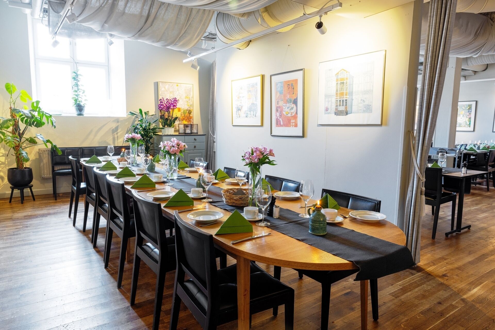 A dining area with a long wooden table set for a meal, surrounded by black chairs.