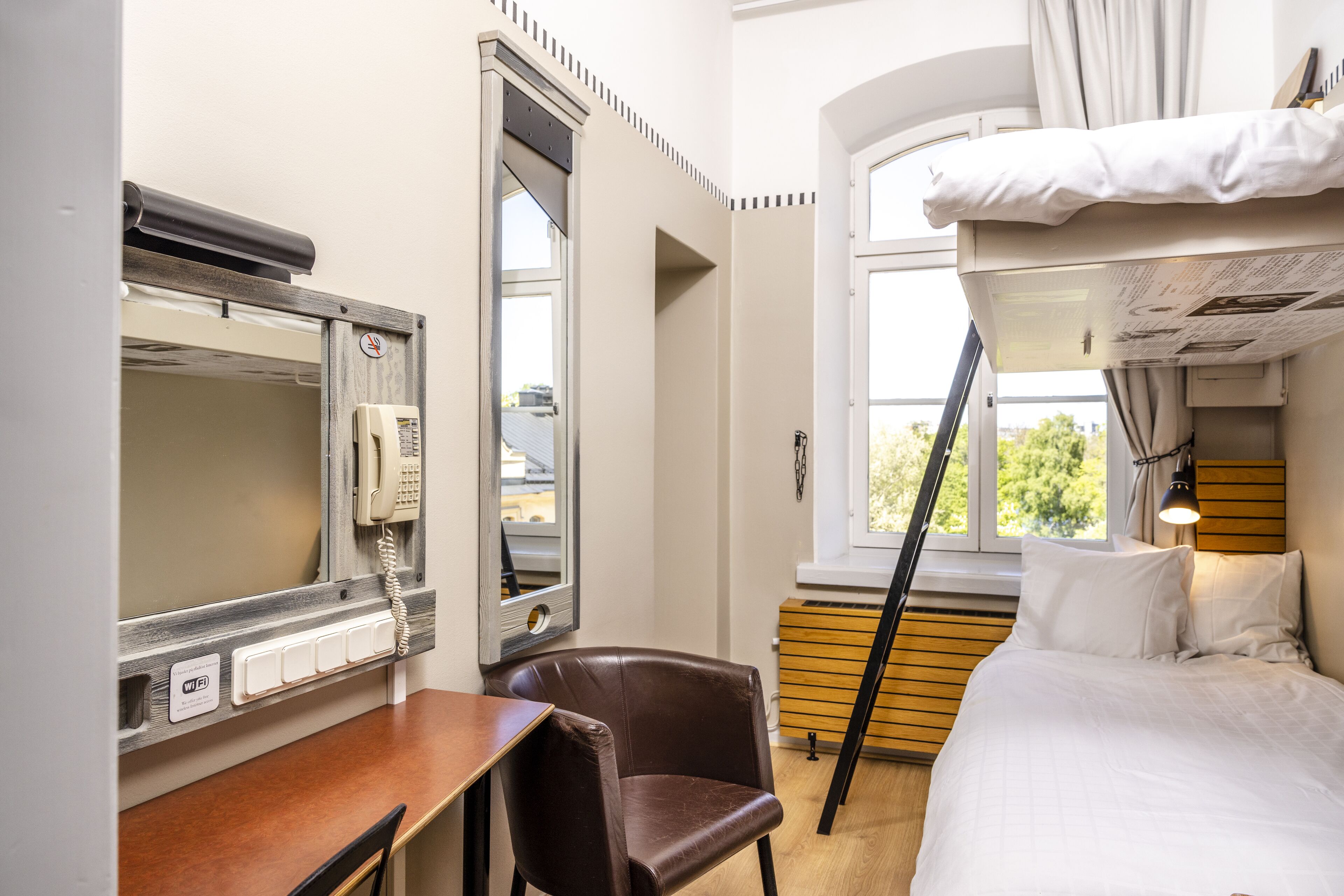 Una habitación de hotel pequeña con literas, un escritorio con teléfono y una silla.