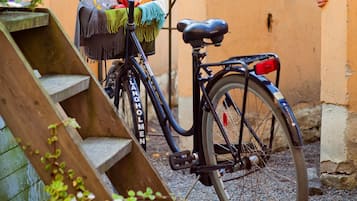 Ein Fahrrad mit Korb und Tasche, abgestellt neben einer Holztreppe und einer Mauer.