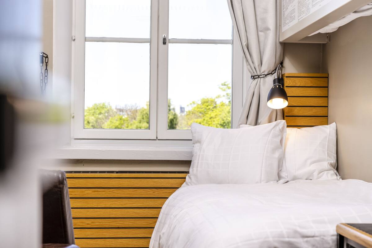 A bedroom with a wooden headboard, white bedding, and a window with curtains.