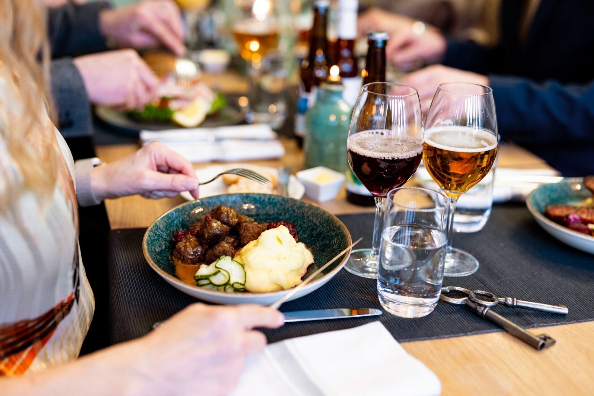 A dining table with plates of food, glasses of beer, and a knife.