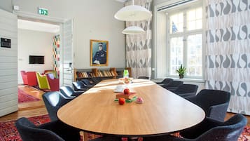 Een vergaderruimte met een lange tafel, stoelen, een boekenkast en een schilderij aan de muur.