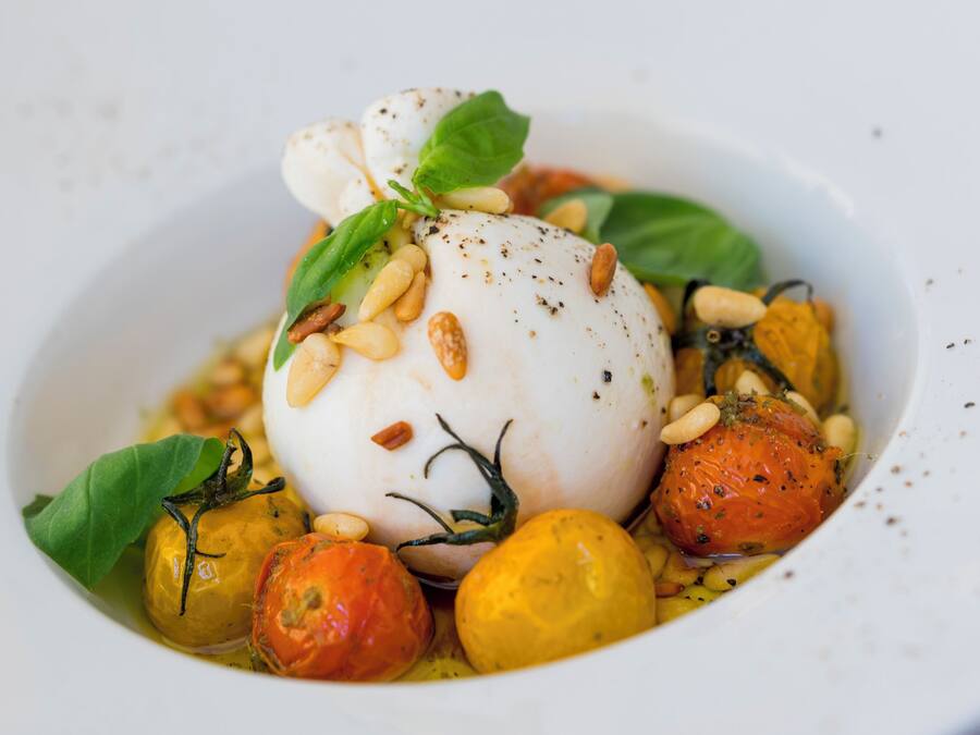 A dish with a white spherical item, tomatoes, and pine nuts on a plate.