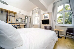 A hotel room with a large bed, a desk with a chair, a television, and a window with curtains.