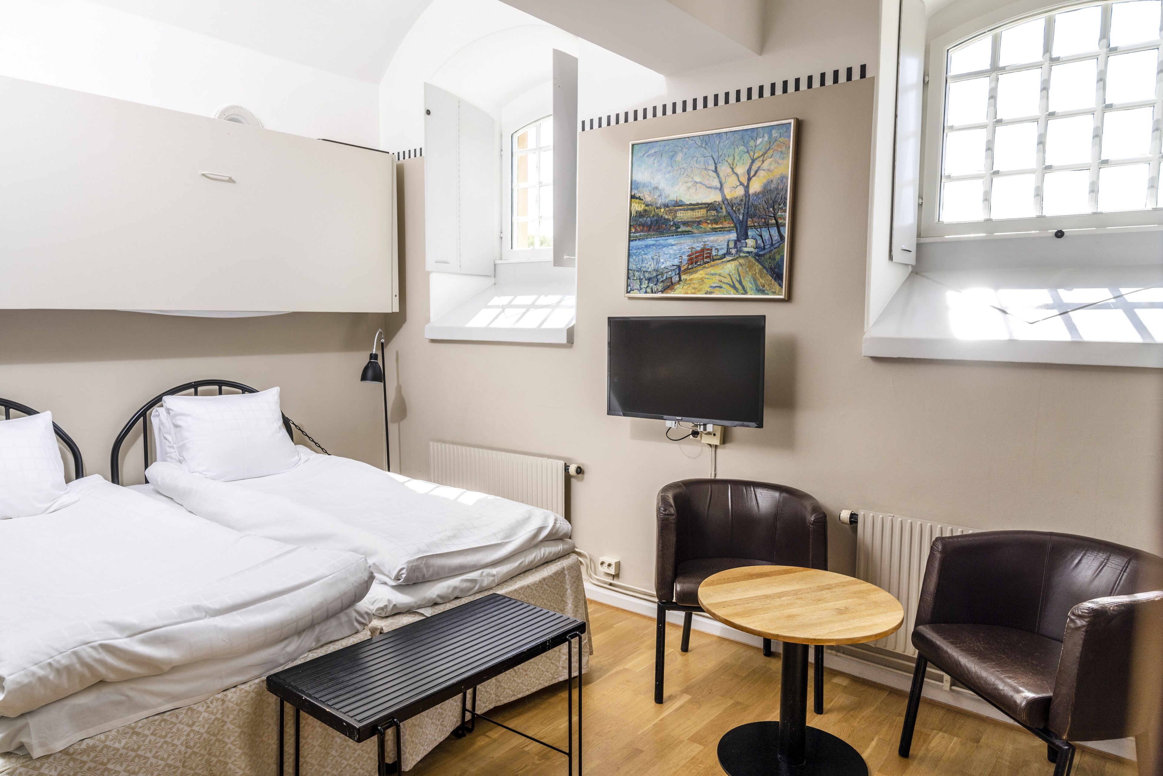 Habitación de hotel con cama, banca, mesa, televisor y un cuadro en la pared.