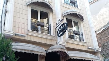 A hotel with a sign reading "PEARL HOTEL," featuring a classic facade with multiple balconies, outdoor seating, and potted plants.