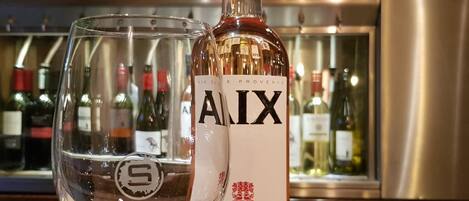 A bottle of AIX wine and a wine glass on a bar counter with various bottles in the background.
