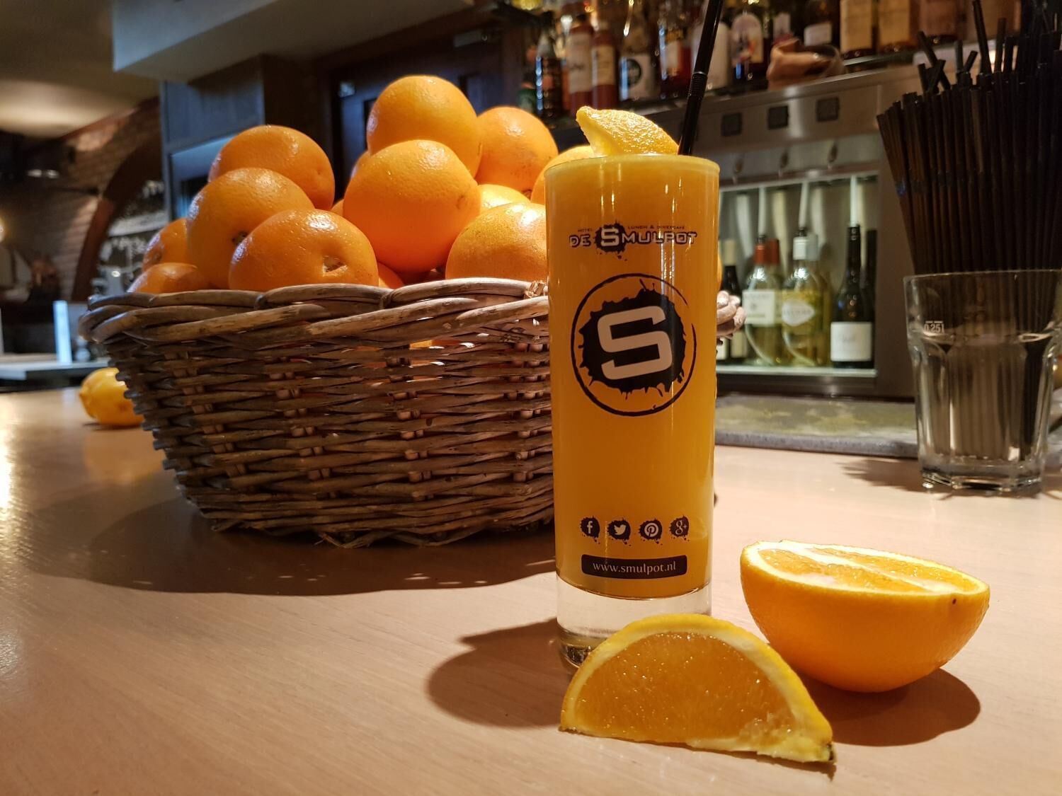 A table with a basket of oranges, a glass of orange juice, and a half orange.