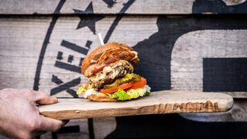 A hand holding a burger on a wooden board.