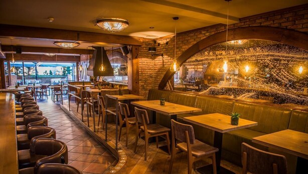 Een restaurantinterieur met houten tafels en zitjes, bakstenen muren en hangende lampen.