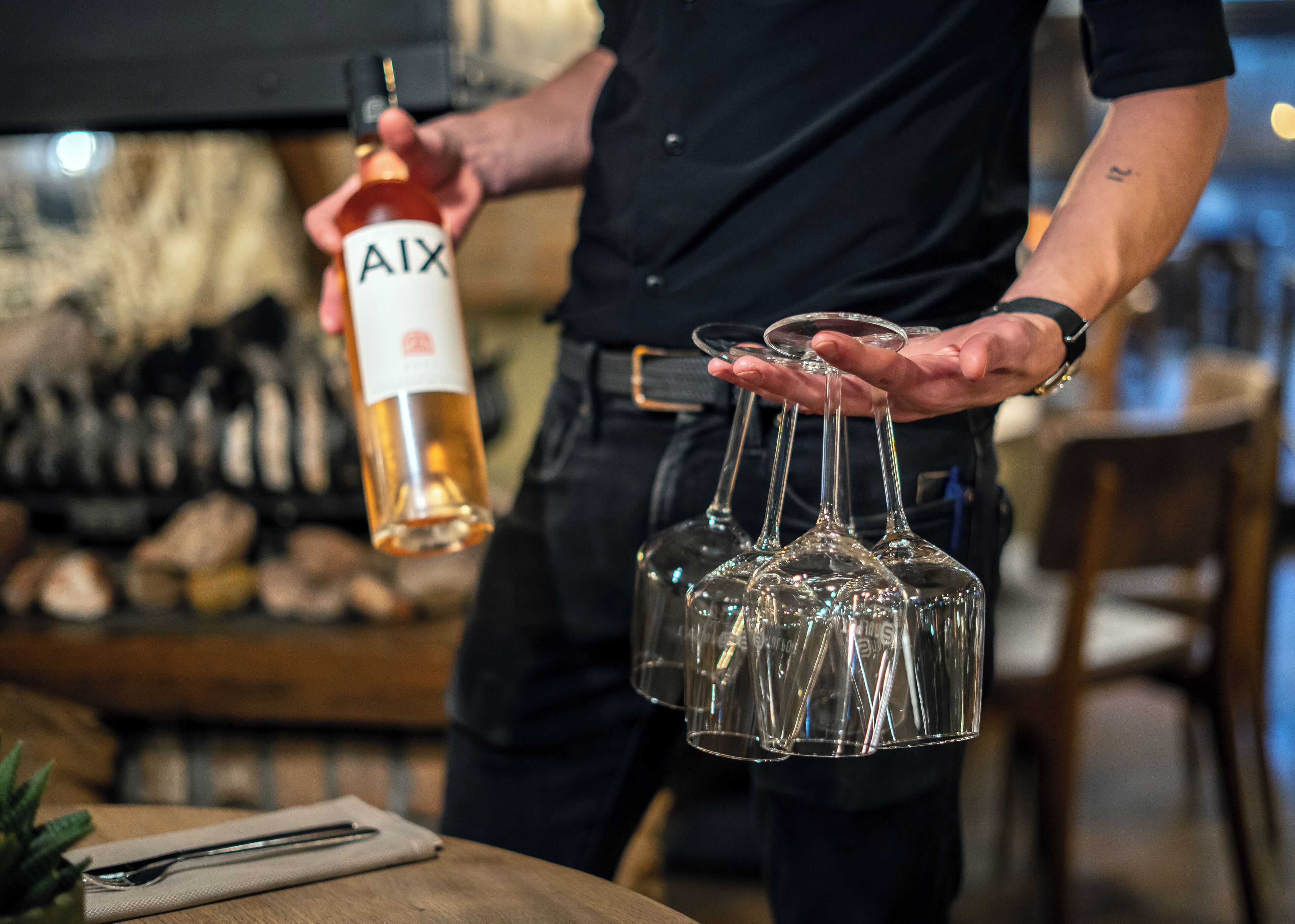 A person holding a bottle of AIX wine and several wine glasses.