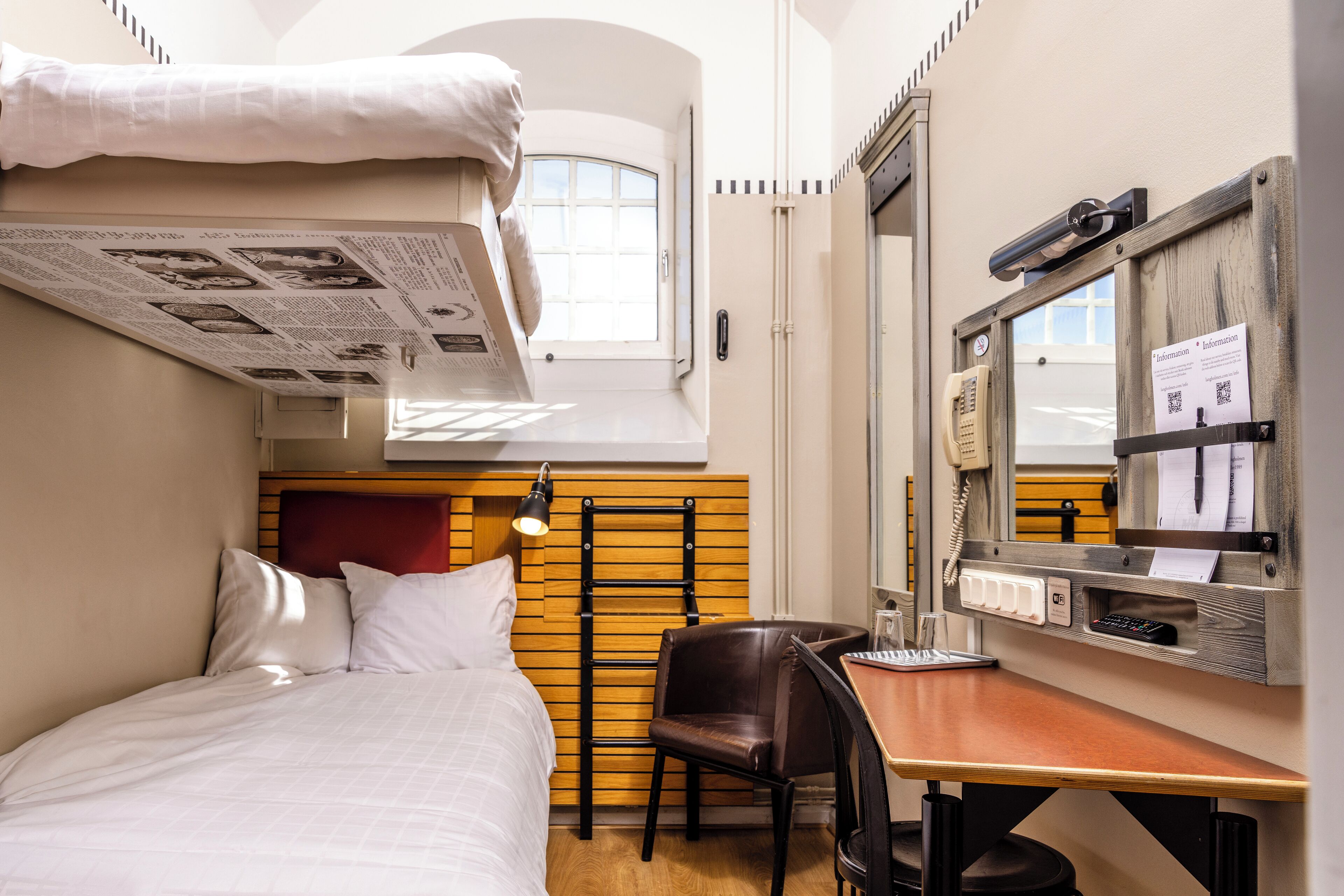 Habitación de hotel compacta con cama, escritorio, silla, espejo y ventana.