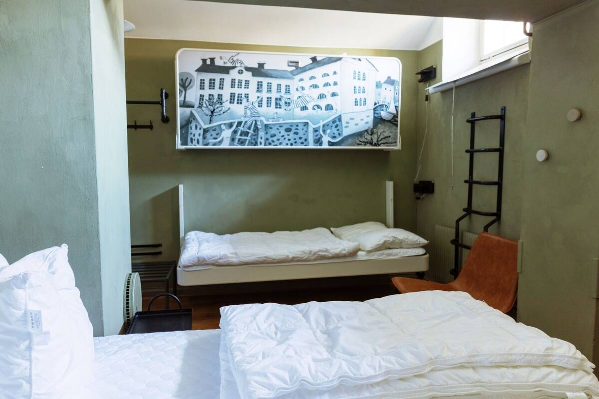 A bunk bed room with a mural of buildings on the wall, a ladder, and a chair.