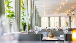 A restaurant interior with long tables, potted plants, and a decorative teapot. - STF Långholmen Hostel (Stockholm)