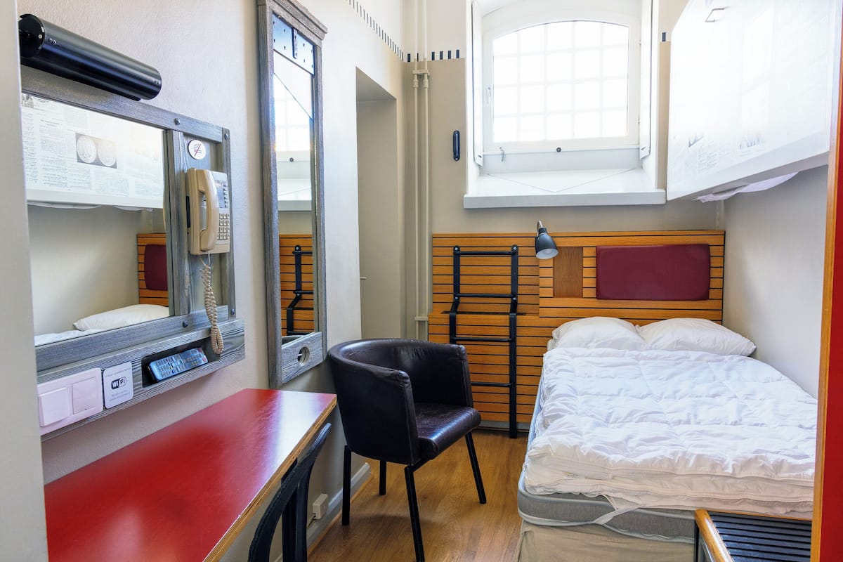 A compact room with a bed, a desk, a chair, a window, and a mirror.