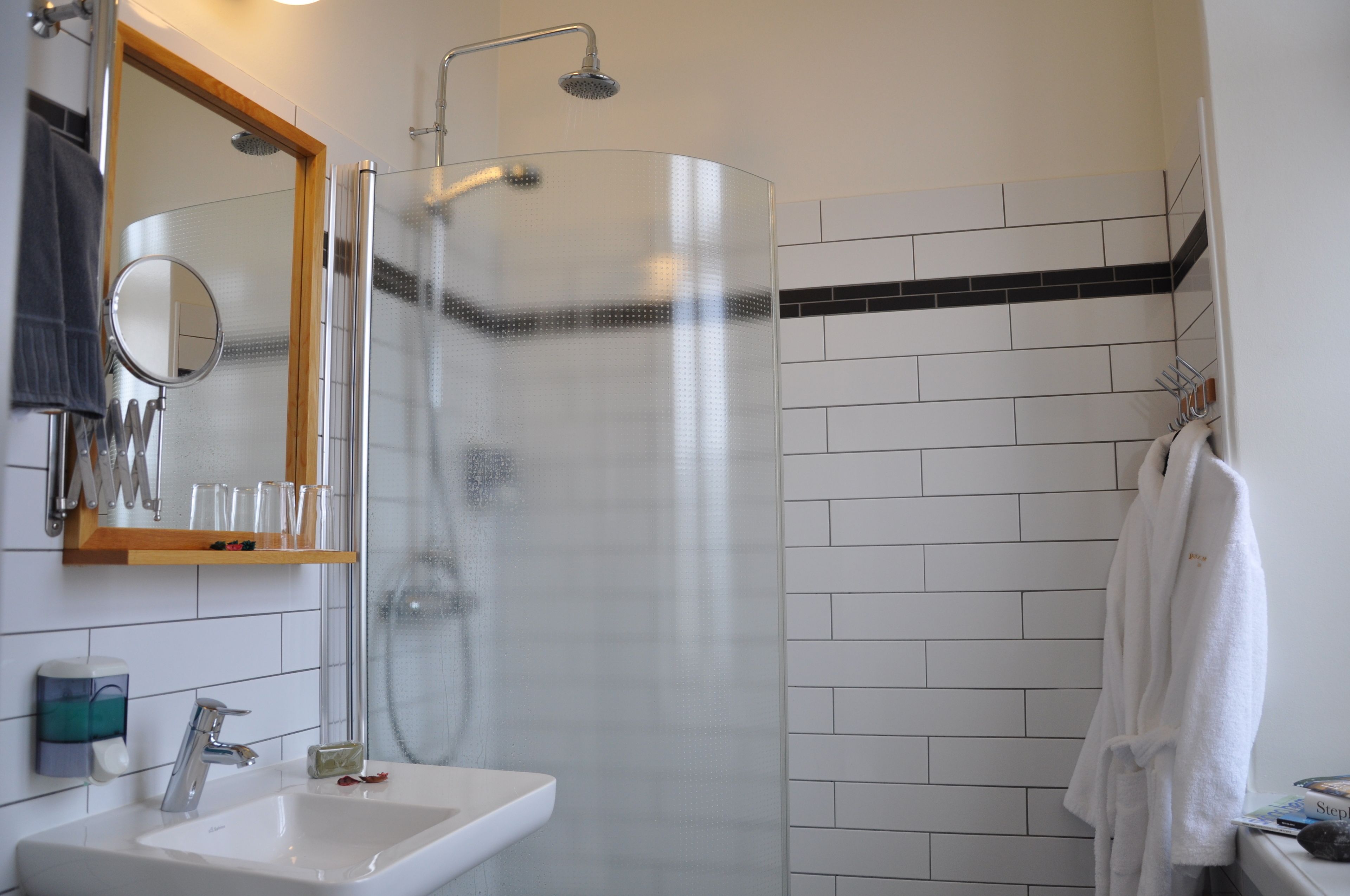 Un baño moderno con ducha envuelta en vidrio, lavamanos con espejo y toallero.