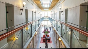 A spacious, well-lit corridor with glass railings, a central seating area with tables and chairs, and a high ceiling with skylights. - STF Långholmen Hostel (Stockholm)