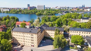 A high-rise building with a flat roof and multiple windows, surrounded by trees and a river. - STF Långholmen Hostel (Stockholm)